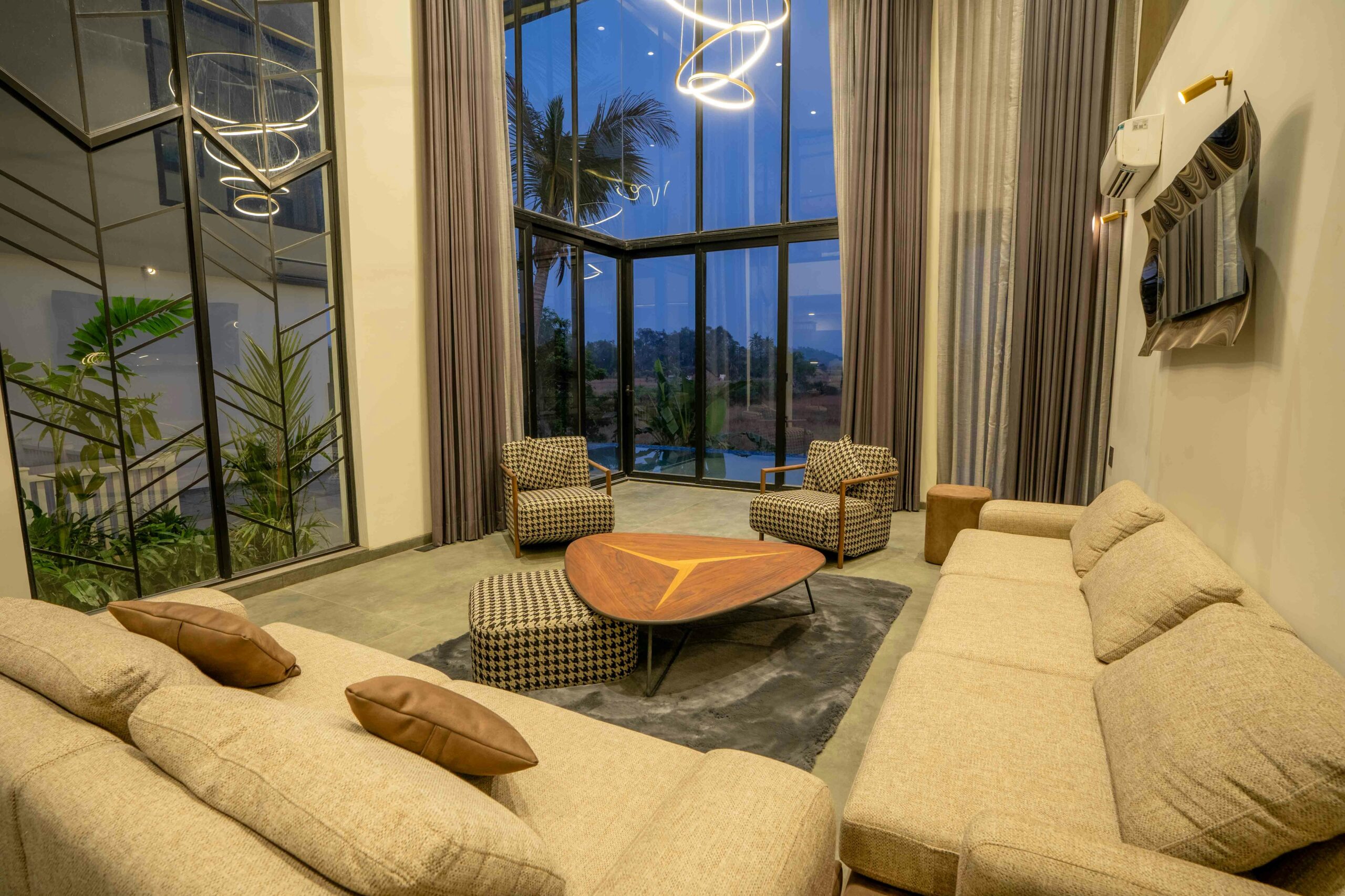 Luxurious living room with modern decor in a villa located in Saligao, India, through large glass windows.